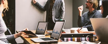 Geschäftsteam in einer Sitzung mit Laptops, die während einer Präsentation Diagramme zeigen.